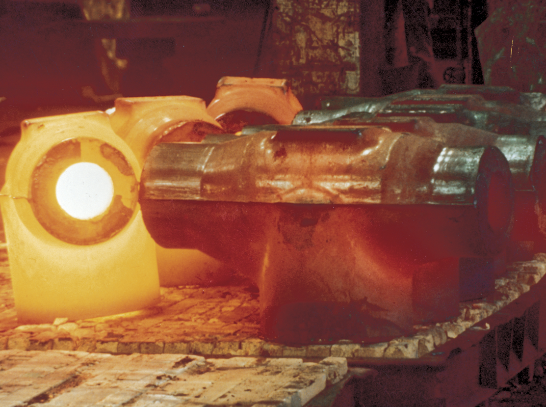 Molten metal in a furnace, glowing brightly. The scene depicts metal components in various stages of heating, with some parts appearing red hot, while others have a cooler, metallic appearance. The industrial setting suggests a manufacturing or foundry environment.